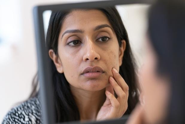 Woman with dehydrated skin looking in the mirror at Sculpt by Kelly Swann in Beaconsfield